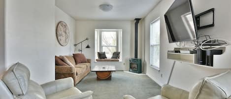 A living room with a sofa, two chairs, a coffee table, a map on the wall, a television, and a fireplace.