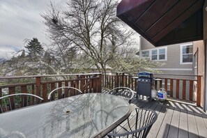 A deck with a glass table and chairs, a barbecue grill, and a propane tank.