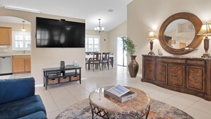 Amplia sala de estar con televisor de pantalla plana, un sofá azul, una mesa de centro, una zona de comedor con sillas y un espejo grande.