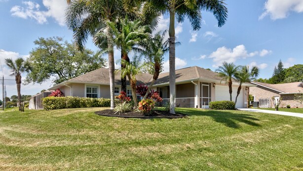 Una casa residencial con césped cuidado, palmeras y diversas plantas florecientes.
