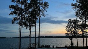 A swimming pool with lounge chairs, surrounded by tall trees, overlooking a body of water at dusk. - Lakeside Retreat Entire House Inground pool, kayaks, dock (Cross Hill)