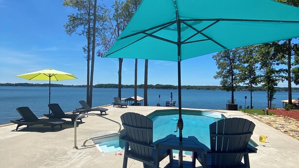 A poolside area with a table and chairs, a yellow umbrella, and a view of a lake. - Lakeside Retreat Entire House Inground pool, kayaks, dock (Cross Hill)