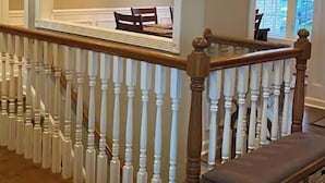 A staircase with white balusters and a wooden handrail, leading to a landing with a bench and two framed pictures on the wall. - Lakeside Retreat Entire House Inground pool, kayaks, dock (Cross Hill)