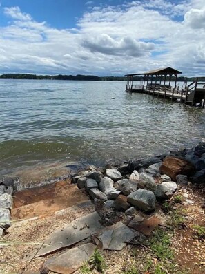 Vista de un lago con un muelle que se adentra en el agua, rodeado de rocas y un césped.