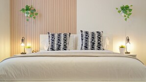 A neatly made bed with white bedding and black and white patterned pillows, flanked by two bedside tables with lamps and small potted plants.