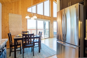 A wooden interior with a dining table, chairs, a refrigerator, and a large window.