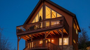 Una baita di legno a due piani con un balcone, ampie finestre e fondamenta in pietra.