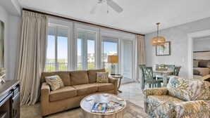 A spacious living room with a large window, a ceiling fan, a dining area, and a view of the outdoors. - Grand Sandestin by Baytowne Wharf Village at Sandestin Golf & Beach Resort.   (Miramar Beach)