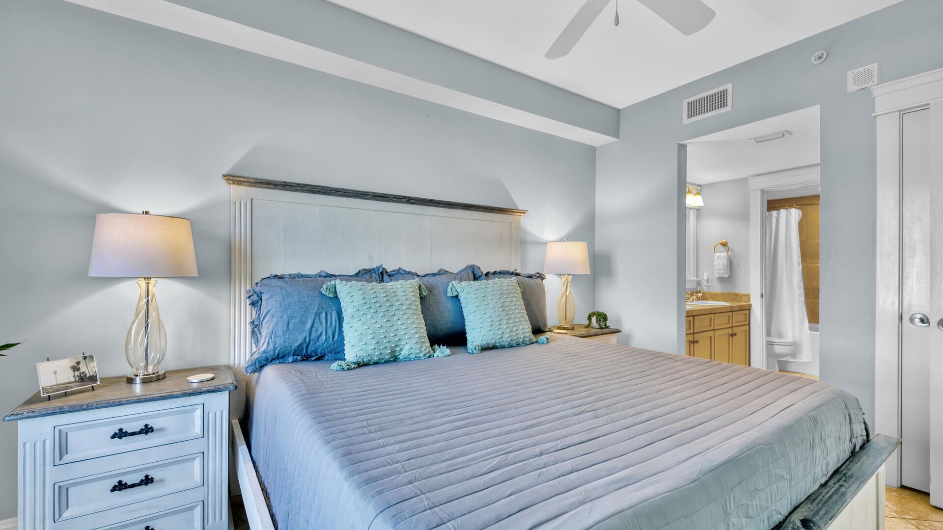 A bedroom with a bed, bedside tables, a nightstand, a dresser, and a bathroom visible through an open door.