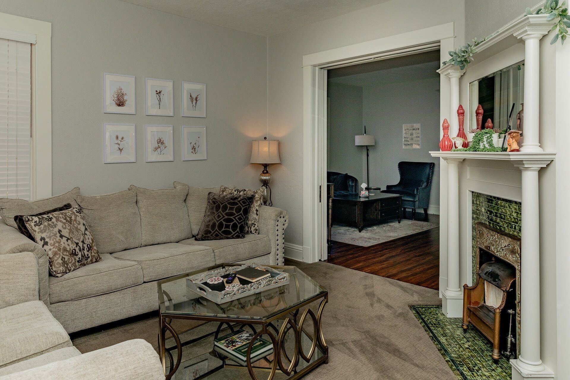 A living room with a beige sofa, a glass coffee table, and a fireplace with decorative items.