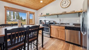 A kitchen with wooden cabinets, a stainless steel refrigerator, and a large clock on the wall. - Avalanche Cabin @ Explorer's Basecamp (Kalispell)
