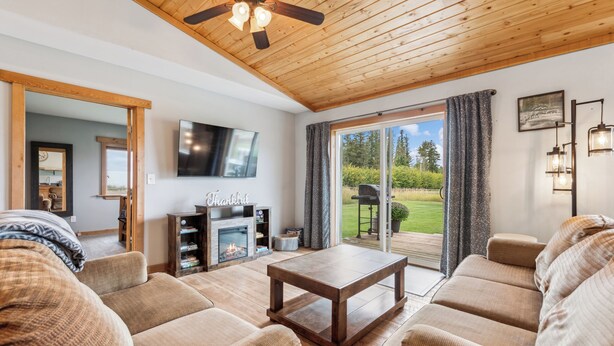 A cozy living room with a fireplace, comfortable sofas, a wooden ceiling, and a large sliding glass door leading to a deck. - Avalanche Cabin @ Explorer's Basecamp (Kalispell)