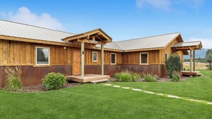 A wooden cabin with a covered porch, a well-maintained lawn, and a clear sky. - Avalanche Cabin @ Explorer's Basecamp (Kalispell)