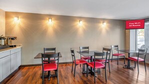 Un comedor con mostrador de cocina, cuatro mesas y seis sillas con cojines rojos.