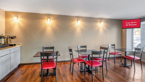 A dining area with a kitchen counter, four tables, and six chairs with red cushions. - Red Roof Inn Richmond - Airport/ Sandston (Sandston)