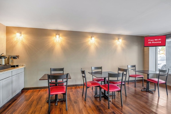 Un espace repas comprenant un comptoir de cuisine, quatre tables et six chaises dotées de coussins rouges.
