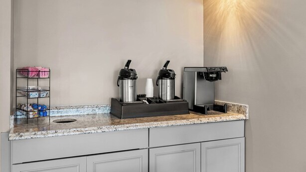 A kitchenette with a coffee maker, two thermos flasks, a cup holder, and a small shelf with items.
