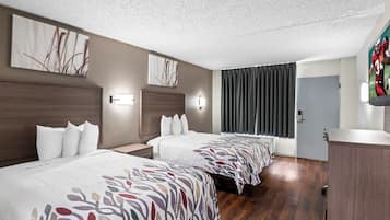 A hotel room with two beds, a wooden headboard, a large window with curtains, and artwork on the walls.