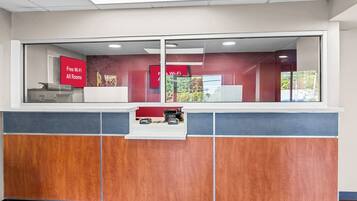 A reception desk with a glass partition, a red sign indicating free Wi-Fi, and a view of the outside.