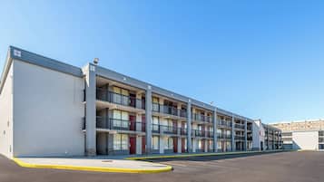 Un motel de varios pisos con una fila de balcones, un estacionamiento y un cielo azul despejado.