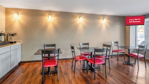 A dining area with a kitchen counter, four tables, and six chairs with red cushions. - Red Roof Inn Richmond - Airport/ Sandston (Sandston)