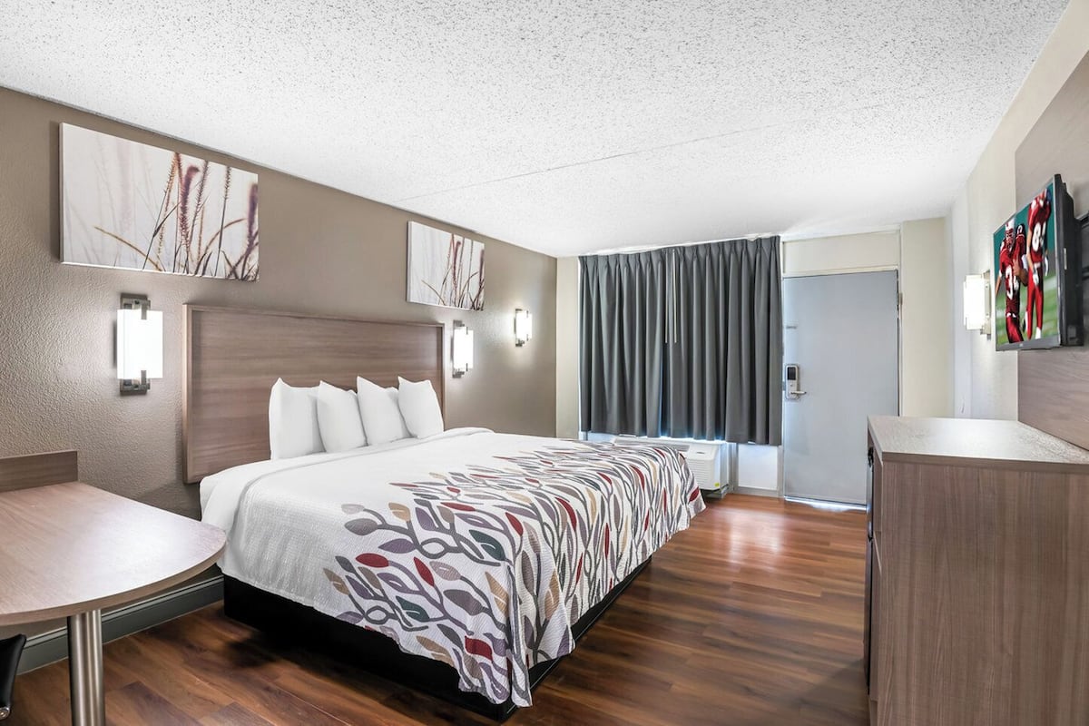 A hotel room with a large bed, a desk, a wardrobe, and artwork on the walls.