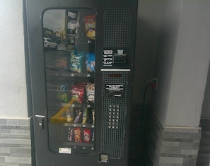 Un distributeur automatique proposant des collations, muni d’une fente pour les pièces et d’un distributeur de monnaie.