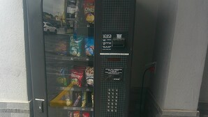 Máquina expendedora con opciones de aperitivos, ranura para monedas y dispensador de cambio.