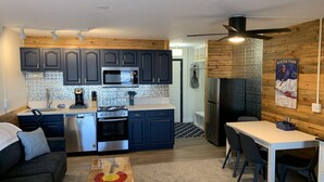 Une cuisine de taille réduite, dotée de meubles de couleur sombre, d’appareils électroménagers en acier inoxydable et d’un mur décoratif en bois.
