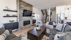A modern living room with a stone fireplace, built-in TV, and a staircase leading to an upper level. - 4bed 5bath brand new beach house in Tiny! West Exposure! Sunsets! Hot tub! (Tiny)