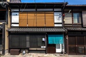 A traditional Japanese building with a closed shutter, a small bench, and a blue cloth hanging over the entrance.