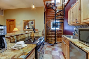 Une cuisine avec un escalier en colimaçon en bois, une cuisinière, un évier et des armoires en bois.