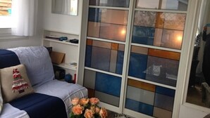 Ein Wohnzimmer mit einer Couch, einem Zierkissen, einer Blumenvase und einem Fenster mit farbigen Scheiben.