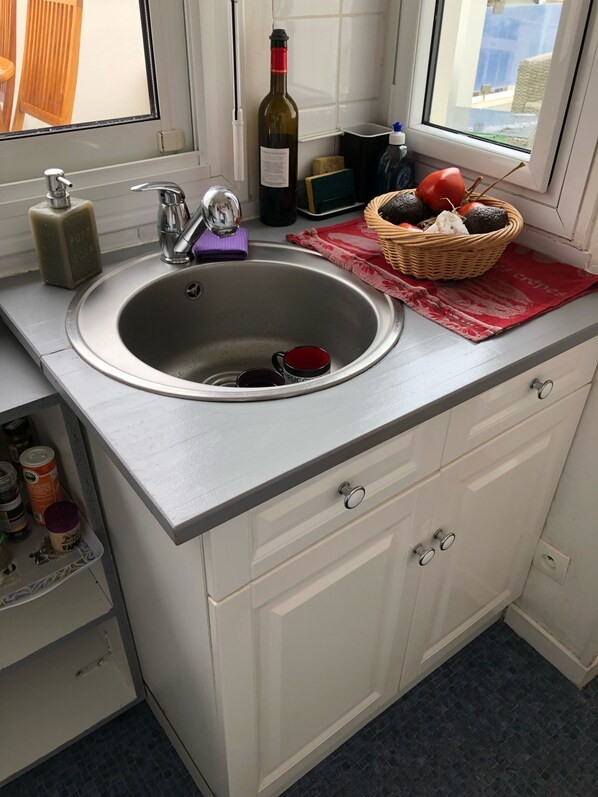 A kitchen with a stainless steel sink, a bottle of wine, and a basket of fruits on the counter. - Appartement T2 avec grande terrasse sans vis à vis au centre d'Arcachon (Arcachon)