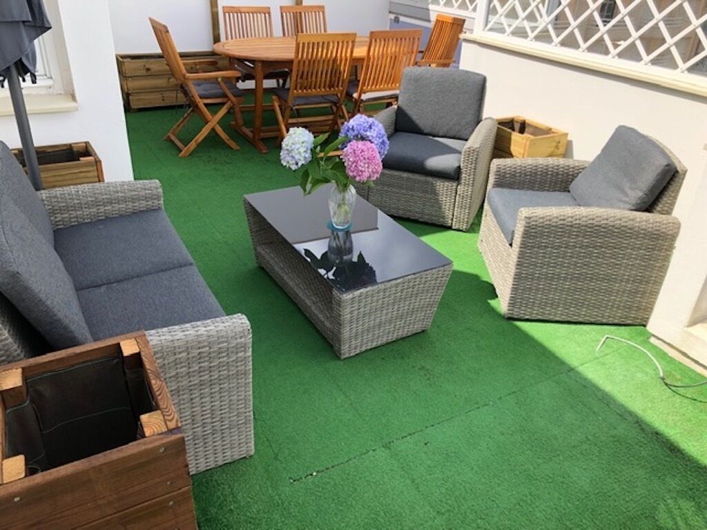 Eine Terrasse mit Korbmöbeln, einem Glastisch und einem Blumenvasen.