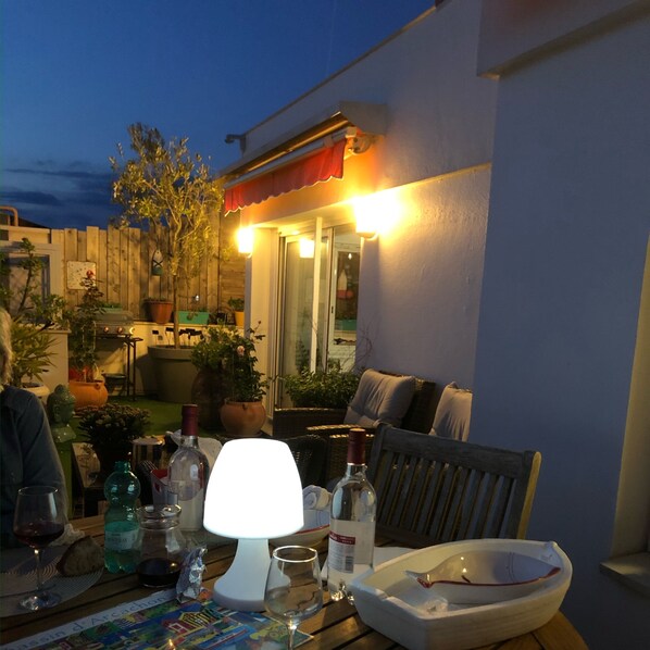 An outdoor patio area with a table set for dining, including wine glasses, bottles, and a bowl. There are potted plants and a wooden fence in the background. - Appartement T2 avec grande terrasse sans vis à vis au centre d'Arcachon (Arcachon)
