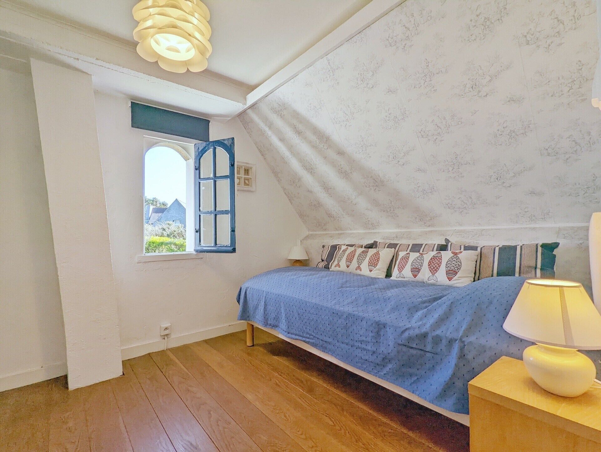 Ein Schlafzimmer mit Bett, Fenster, Lampe und Holzboden.