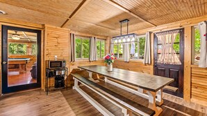 A wooden interior with a large table, benches, a microwave, and a door leading to an outdoor area.