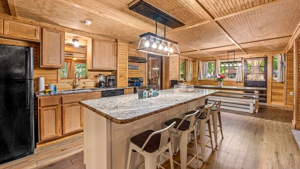 A spacious kitchen with wooden cabinets, a large island with bar stools, and a hanging light fixture.