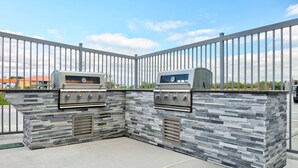 Eine Außenküche mit zwei Gasgrills, einer Steinrückwand und einem Metallzaun.