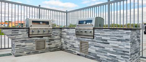 An outdoor kitchen with two gas grills, a stone backsplash, and a metal fence.