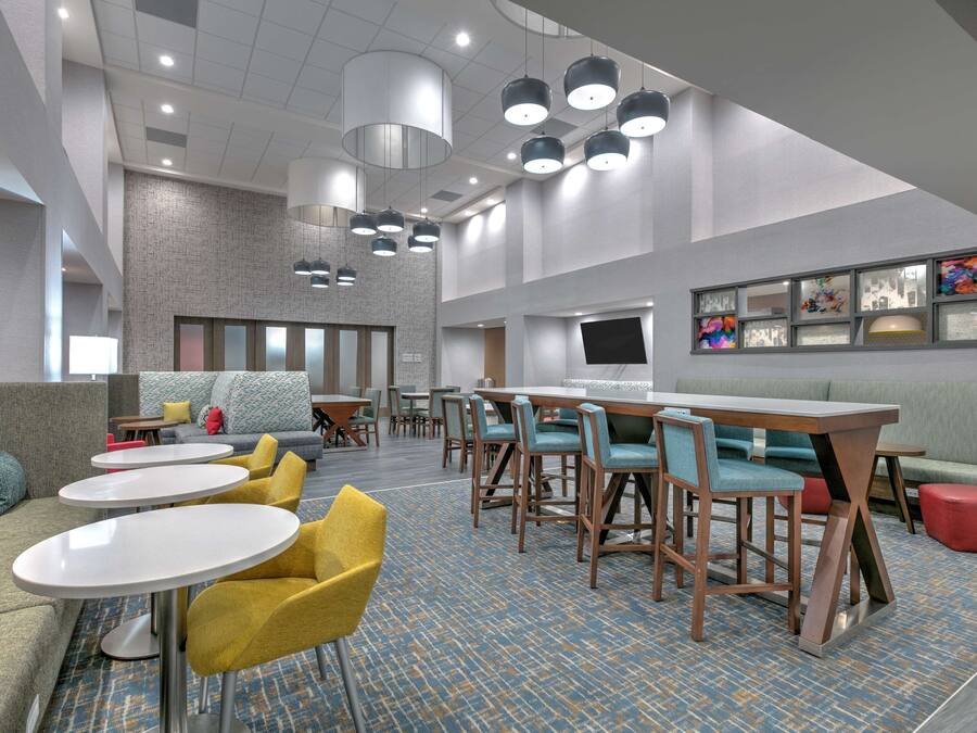 Een moderne hotel lobby met ronde tafels, comfortabele zitmogelijkheden en een groot televisiescherm.