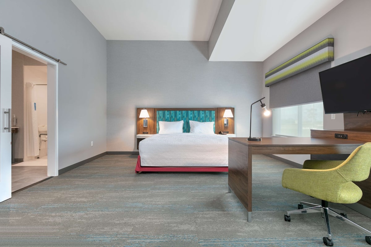 A hotel room with a bed, desk, chair, and TV.