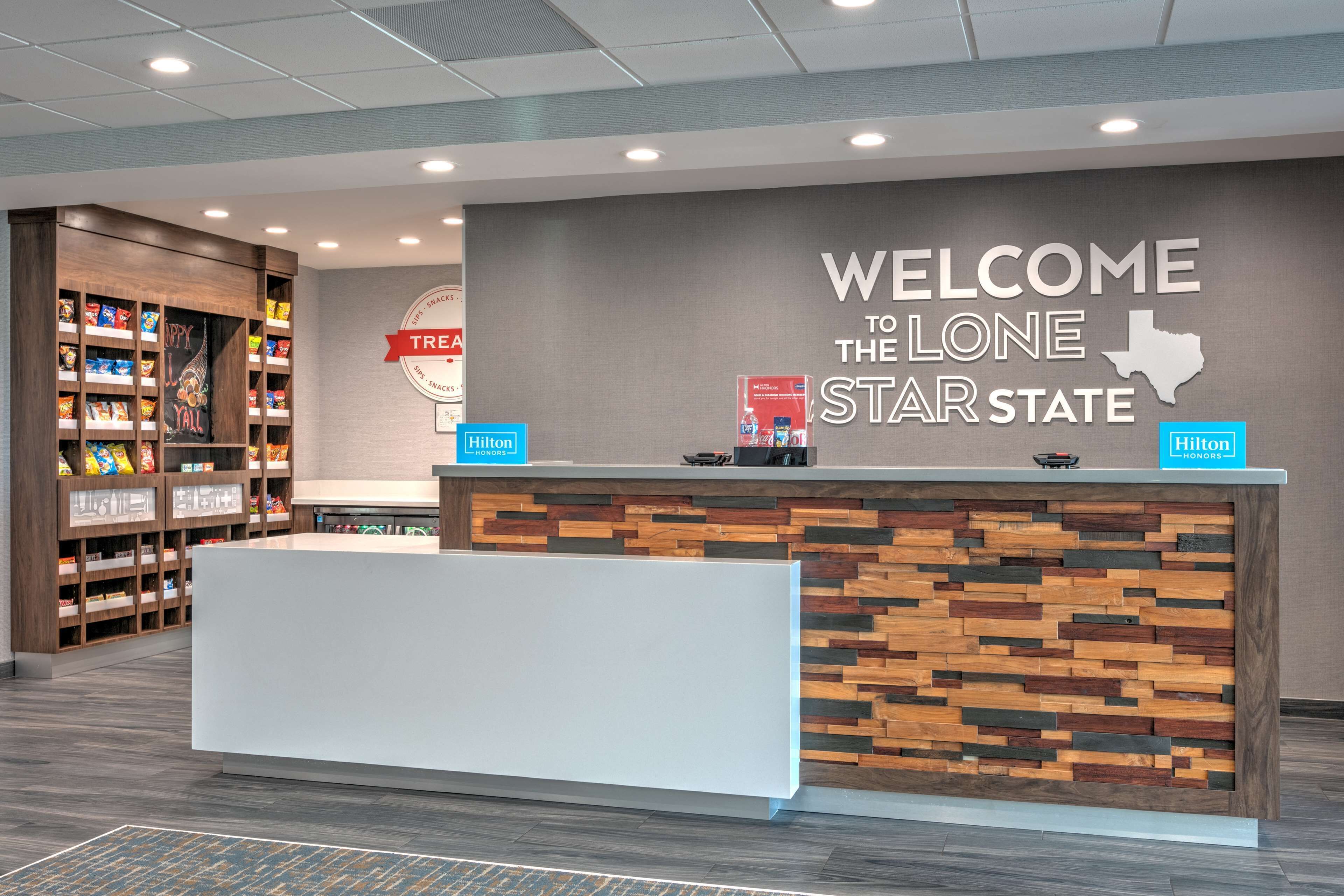 Et hotellets receptionområde med en velkomstskilt, hylder med snacks og et Hilton Honors skilt.