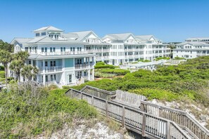 A coastal hotel with multiple-story buildings, balconies, and a wooden boardwalk leading to the beach.