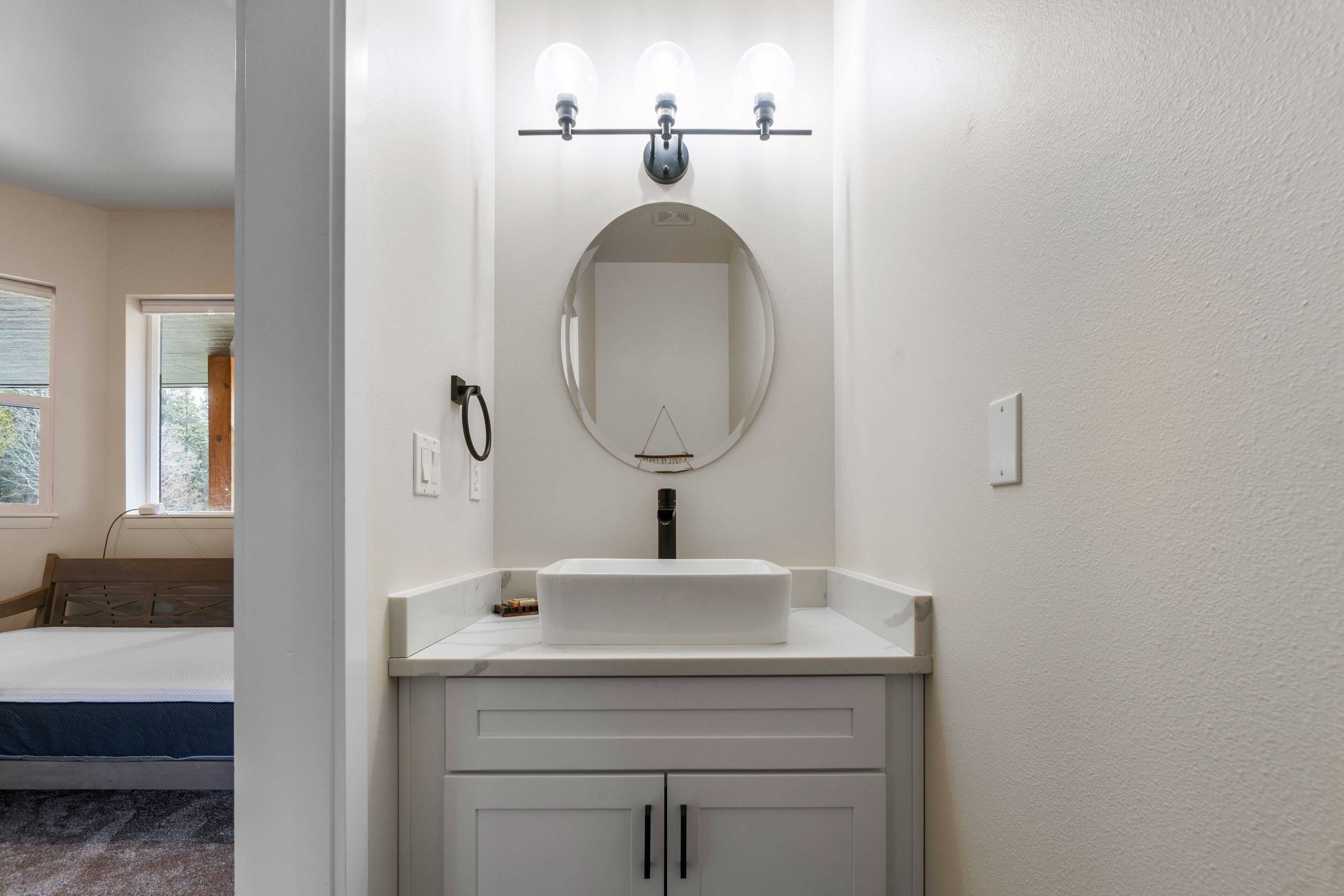 A bathroom with a white vanity, a round mirror, and a lighted vanity mirror.