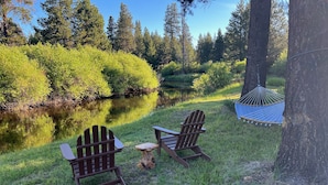 Two Adirondack chairs and a hammock near a pond surrounded by trees. - River Front House -20 min to Bend -25 min to Mt Bachelor - Sleeps 12 (Bend)