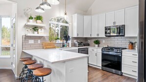 A modern kitchen with white cabinets, a large island with stools, a built-in oven, and a microwave. - River Front House -20 min to Bend -25 min to Mt Bachelor - Sleeps 12 (Bend)