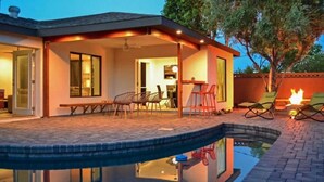 A swimming pool with a covered patio area, outdoor seating, and a fire feature.