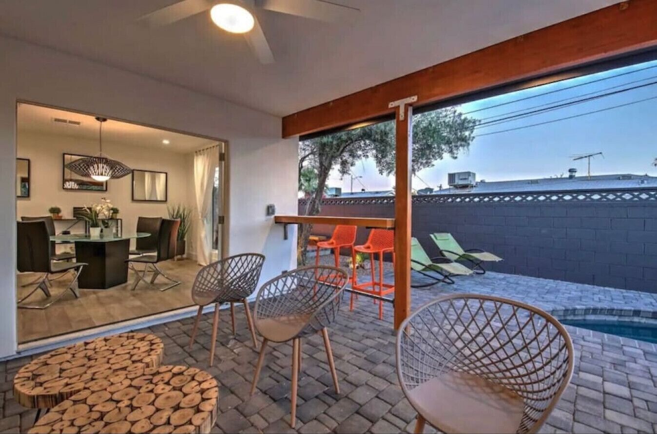 Un patio moderno al aire libre con piscina, sillas de mimbre y un comedor con barra.
